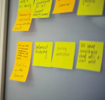 A close-up, angled view of a whiteboard covered in yellow sticky notes featuring handwritten project notes and brainstorming ideas. Some notes are in sharp focus while others blur toward the edges, capturing the dynamic atmosphere of an active design or planning session.